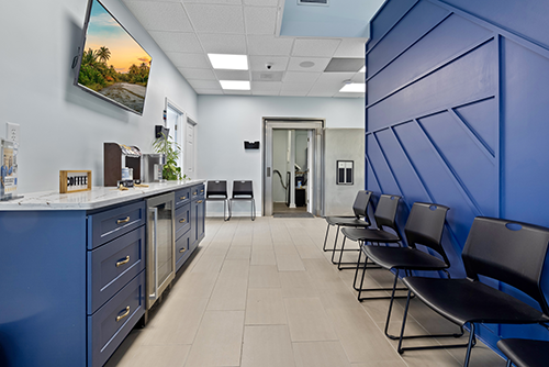 Dalton waiting area with a blue accent wall, modern seating, a coffee station and a wall-mounted TV.