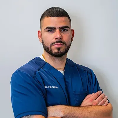 Dr. Wilfredo Sánchez, Doctor of Chiropractic at Inspine Chiropractic, wearing blue scrubs with arms crossed.