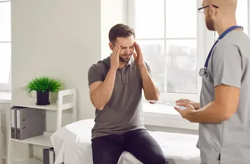 A man holding his head during a consultation with a clinician.