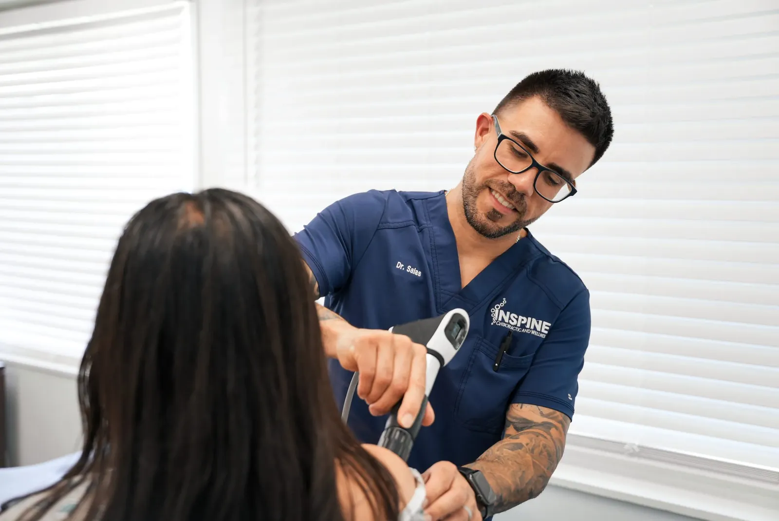 A clinician treating a patient's shoulder with a shockwave therapy handpiece.