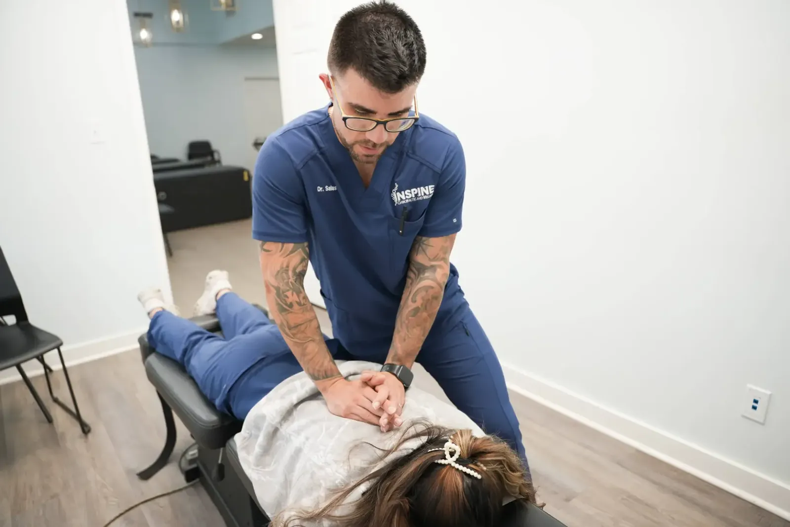 A chiropractor delivering a mid-back adjustment to a patient on a treatment table in a bright clinic room.