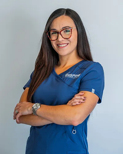 Dr. Natalia Vega, co-owner of Inspine Chiropractic, smiling in a blue scrubs uniform.