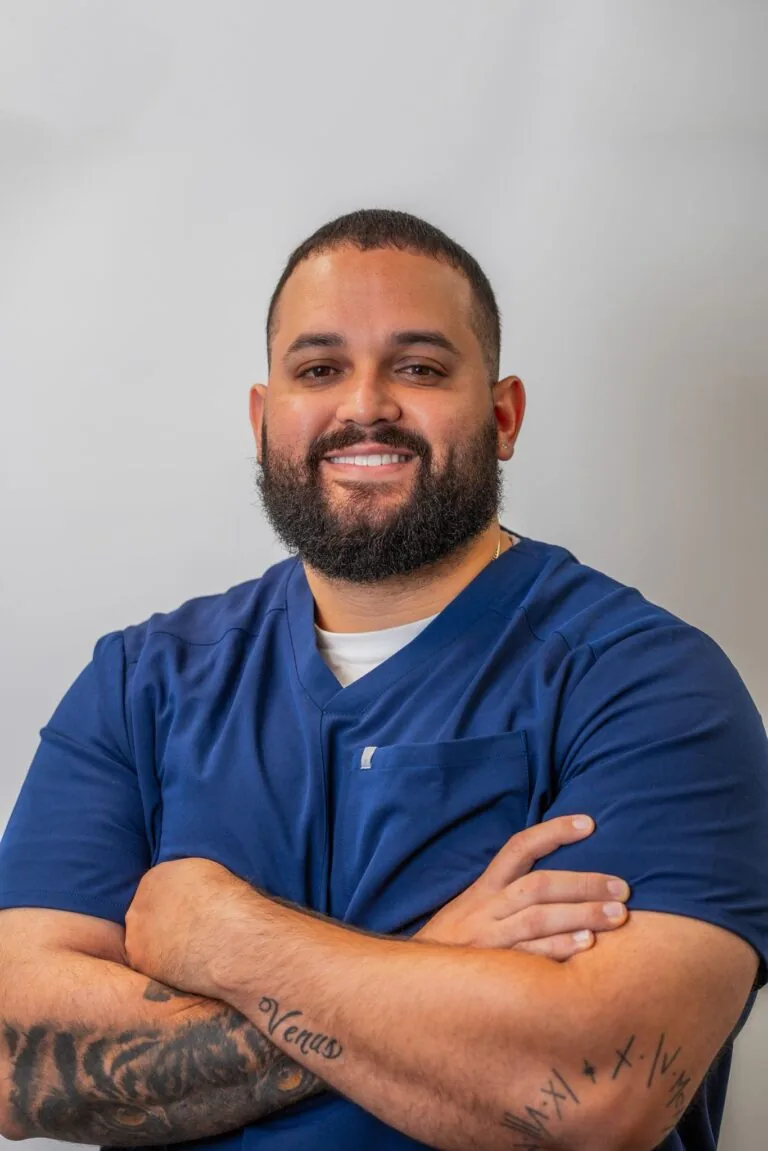 Dr. Roberto Santa, chiropractor at Inspine Chiropractic and Wellness, smiling with arms crossed and wearing a blue scrub top.