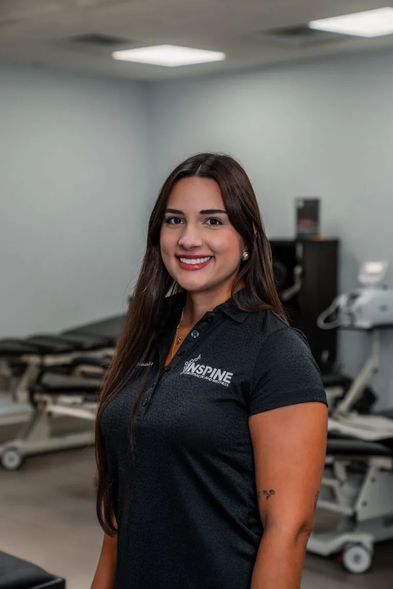 Dr. Tiffany Hernandez, chiropractor at Inspine Chiropractic and Wellness, smiling in a clinic setting with treatment tables in the background.
